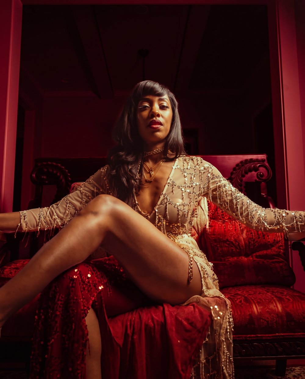 Gigi Da Beast seated on a red velvet throne in a gold sequin dress