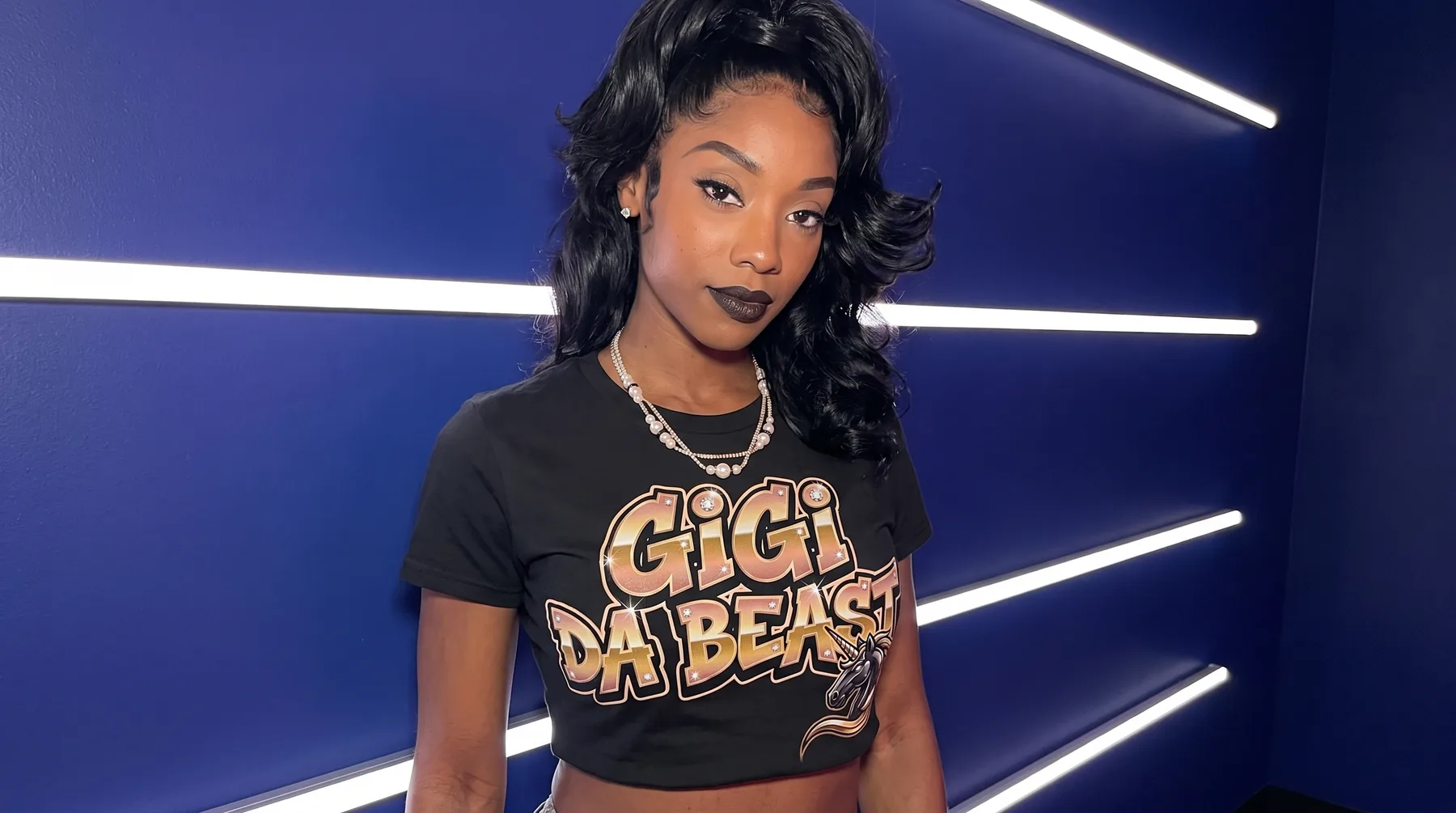 Gigi Da Beast wearing the black Gigi Da Beast crop top in front of a blue neon wall
